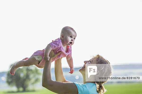Eine fröhliche Mutter hält ihr Baby in der Luft.