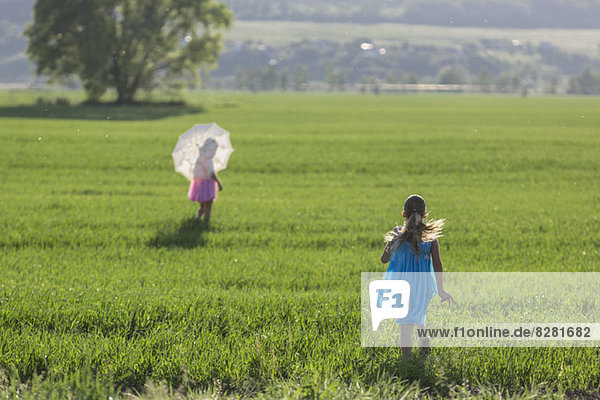 A young girl running to catch up with her twin sister in sunny field