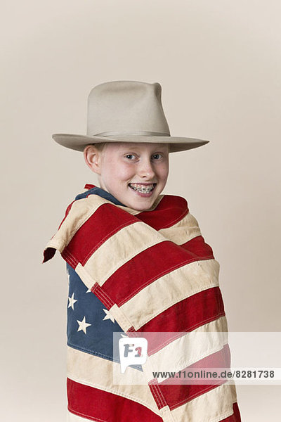 Ein lächelndes Mädchen  das einen Rangerhut trägt und in eine amerikanische Flagge gehüllt ist.