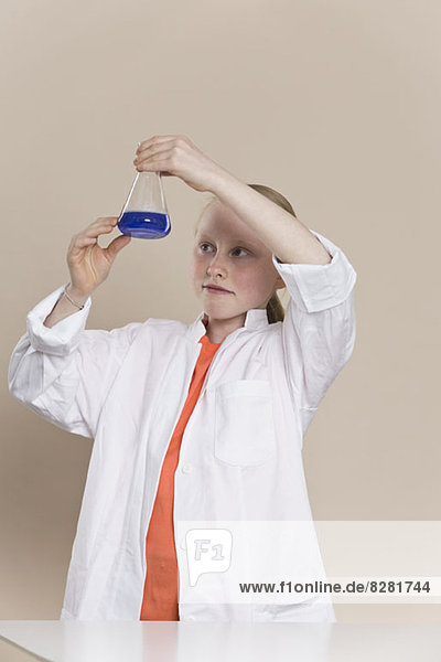 Ein Mädchen  das einen Laborkittel trägt und einen Kegelkolben mit blauer Flüssigkeit darin hält.
