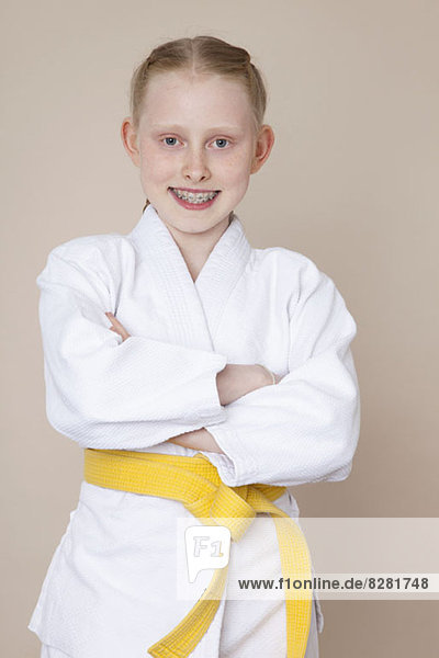 Ein lächelndes Mädchen mit gekreuzten Armen in Kampfsportuniform mit gelbem Gürtel.