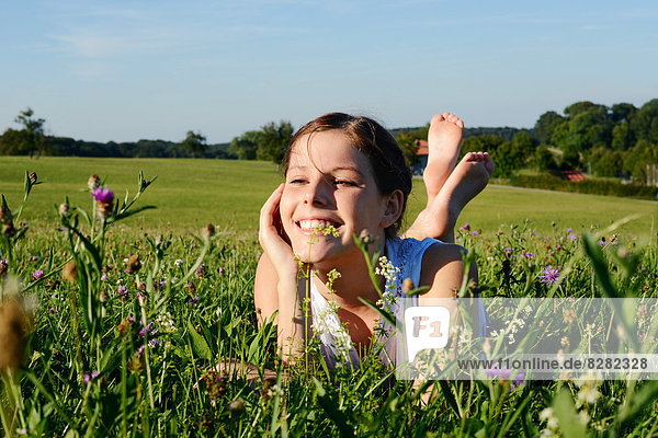 Lächelndes Mädchen liegt in einer Blumenwiese