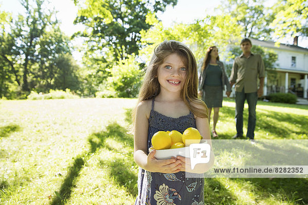 Bauernhof. Kinder und Erwachsene arbeiten zusammen. Ein Mädchen hält eine Kiste mit Zitronen und frischen Früchten. Zwei Erwachsene im Hintergrund.