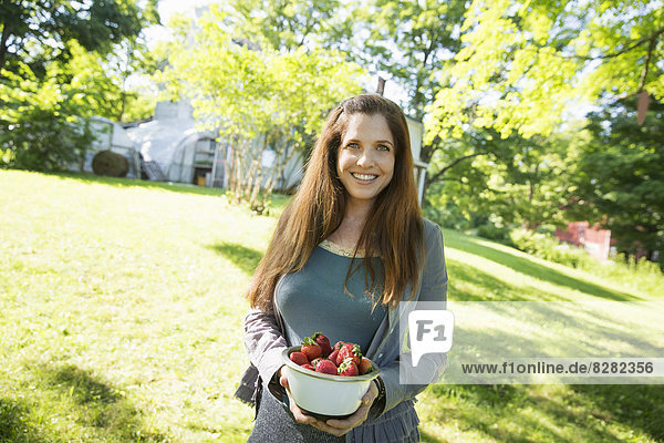 Auf der Farm. Eine Frau trägt eine Schale mit frisch gepflückten Bio-Erdbeeren.