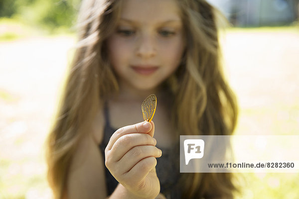Ein junges Mädchen mit langer Blondine  die einen zarten  mit Spitzen gemusterten  ausrangierten Schmetterlingsflügel in der Hand hält.