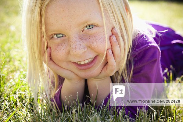 A Young Girl Lying On The Grass On Her Front With Her Chin Resting On Her Hands. Laughing. Close Up.