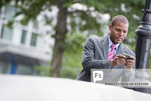 Ein junger Mann in einem Business-Anzug mit blauem Hemd und roter Krawatte. Auf einer Straße in New York City. Mit einem Smartphone.