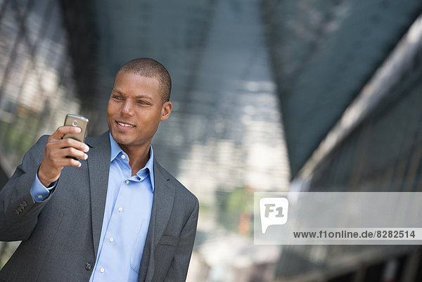 A Businessman In A Suit  With His Shirt Collar Unbuttoned. On A New York City Street. Using A Smart Phone.