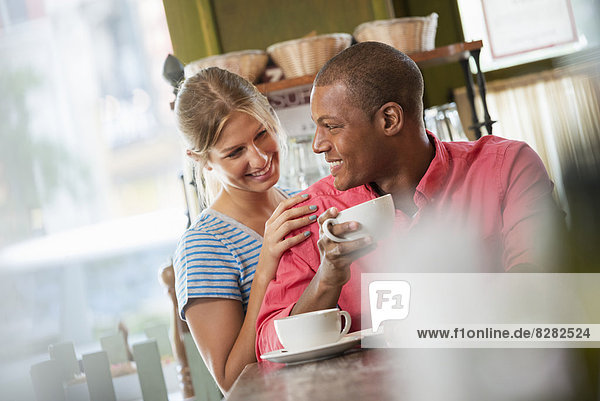 Two People  A Man And Woman Seated Close Together  Looking At Each Other. Having A Cup Of Coffee.