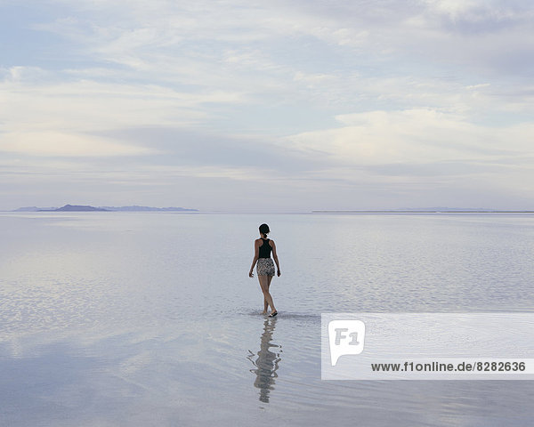 A Woman Standing On The Flooded Bonneville Salt Flats At Dusk. Reflections In The Shallow Water.