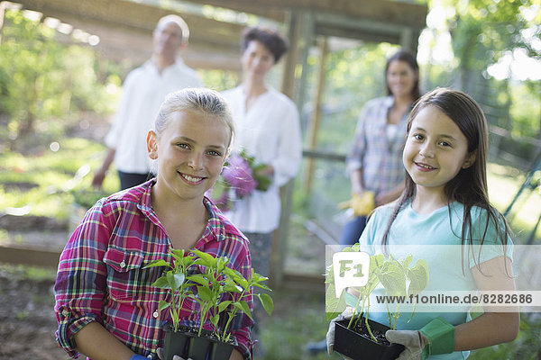 Biologische Landwirtschaft. Sommerfest. Zwei Mädchen sitzen mit jungen Pflanzen  ein reifes Paar und eine junge Frau schauen zu.