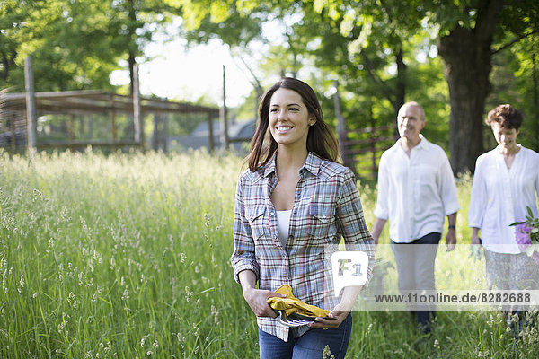 Biologische Landwirtschaft. Sommerfest. Zwei reife Menschen  ein Paar und eine junge Frau beim Spaziergang durch das lange Gras.