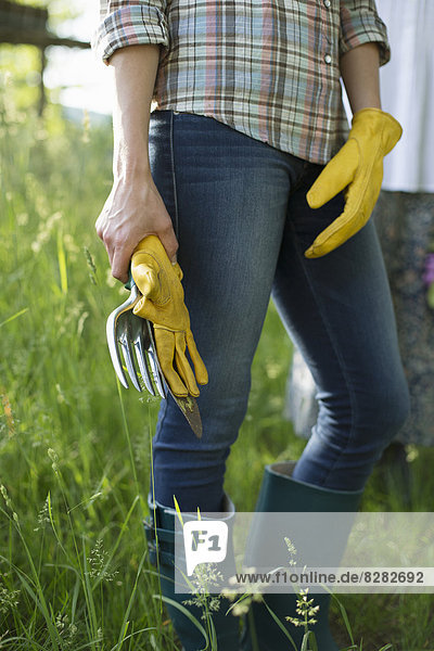 Biologische Landwirtschaft. Ein Arbeiter trägt blaue Jeans,  gelbe dicke Gartenhandschuhe,  die eine Kelle halten.