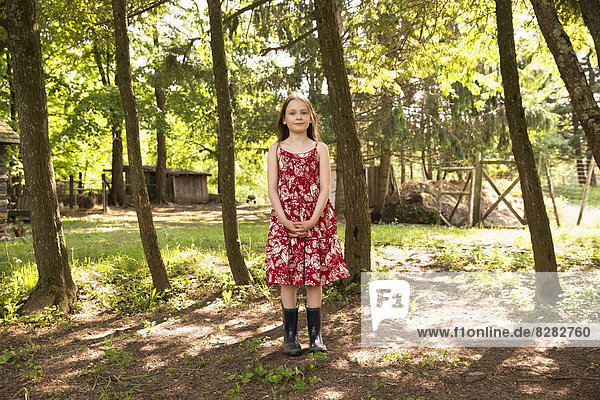 Ein Mädchen in einem Sommerkleid  das in einem Baumhain steht.