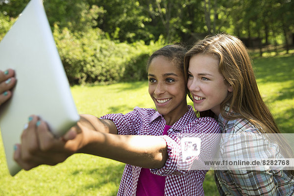 Zwei Mädchen sitzen unter freiem Himmel auf einer Bank und benutzen ein digitales Tablett. Sie halten es auf Armeslänge heraus.