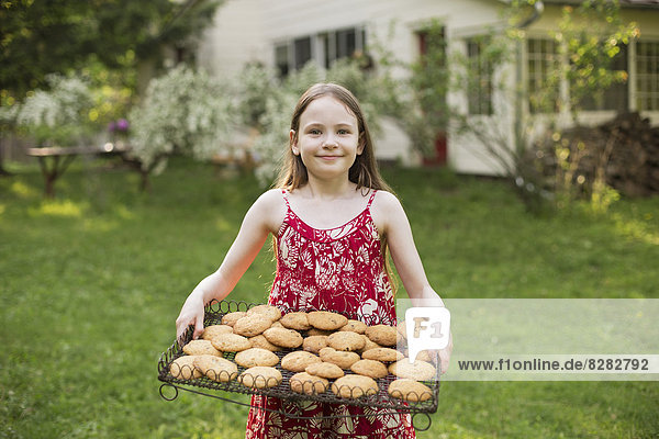 Hausgemachte Kekse backen. Ein junges Mädchen hält ein Tablett mit frisch gebackenen Keksen in der Hand.
