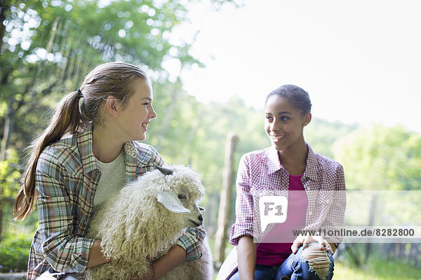 Zwei junge Mädchen auf dem Bauernhof  im Freien. Eine mit ihren Armen um eine sehr flauschig behaarte Angoraziege.