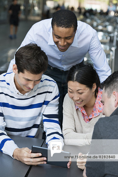 Geschäftsleute in Bewegung. Vier Personen haben sich zu einer Diskussion um ein digitales Tablet versammelt. Ansicht von oben.
