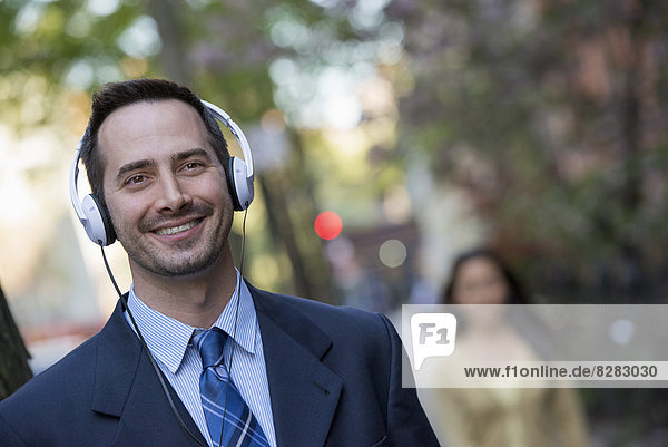 Ein Mann in einem Business-Anzug mit weißen Kopfhörern  der Musik hört.