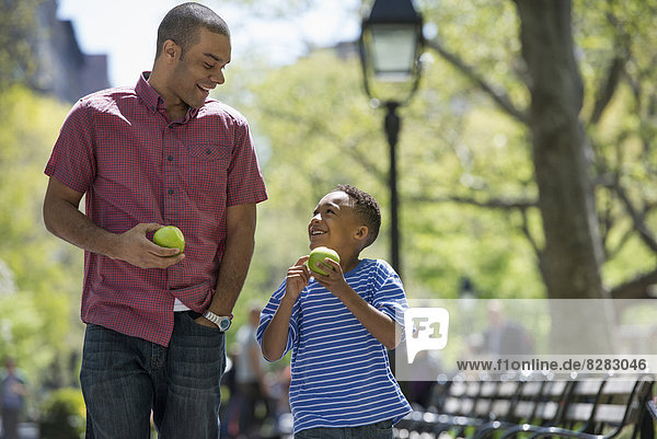 A Family In The Park On A Sunny Day. A Man And A Boy Eating Apples.
