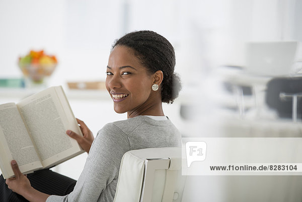Business. A Woman Sitting And Reading A Book. Research Or Relaxation. Looking Over Her Shoulder And Smiling.