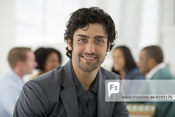 Business Meeting. A Group Sitting Down Around A Table. A Man Smiling Confidently.
