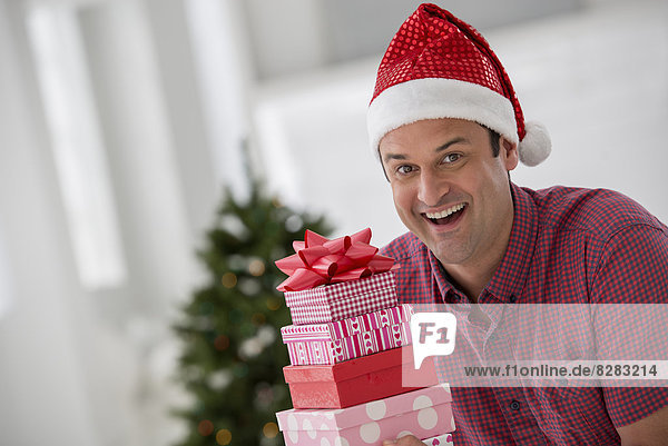 Innenministerium. Wir feiern Weihnachten. Ein Mann in einer Nikolausmütze mit einem Stapel Geschenke. Geschmückter Weihnachtsbaum.
