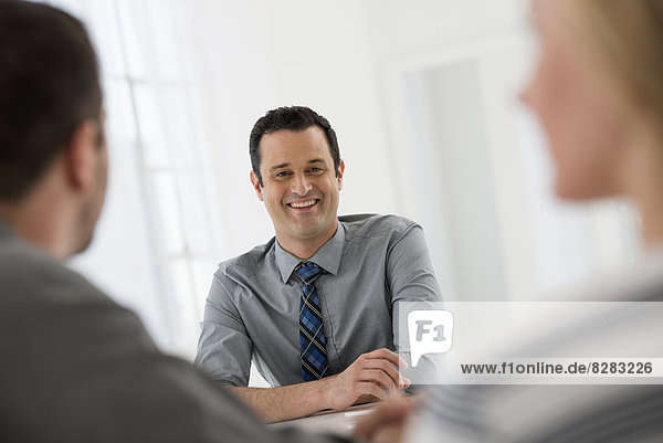 Office Interior. Three People Sitting Around A Table At A Business Meeting.
