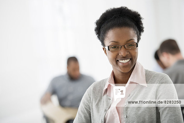Office Interior. A Woman Smiling Confidently. Two Colleagues In The Background.