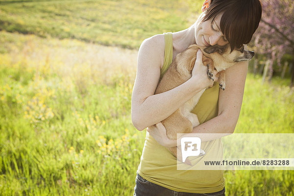 Young Woman In Grassy Field In Spring Holding A Dog