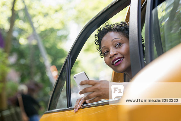 Eine Frau sitzt auf dem hinteren Fahrgastsitz eines gelben Taxis und überprüft ihr Telefon.