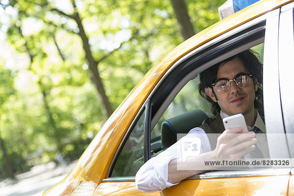 A Young Man In The Back Seat Of A Yellow Cab  Looking At His Smart Phone.