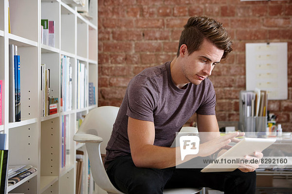 Portrait of young man sitting on chair using digital tablet