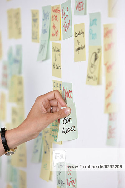 Woman's hand sticking adhesive note saying teamwork on wall