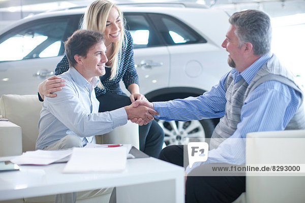 Autoverkäufer und Ehepaar beim Händeschütteln im Autohaus