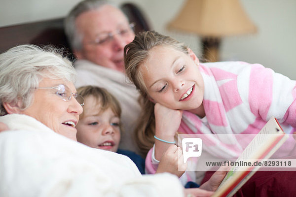 Grandparents and grandchildren reading storybook in bed