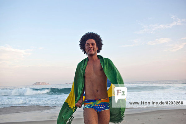 Junger Mann am Strand  in die brasilianische Flagge gehüllt