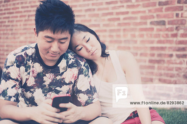 Young couple sitting down in front of brick wall