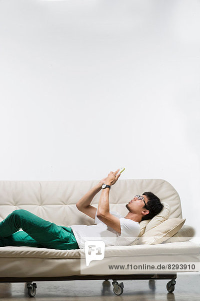 Junger Mann auf dem Sofa liegend mit Smartphone