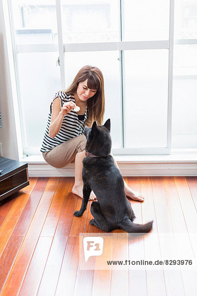 Frau füttert Hund im Wohnzimmer