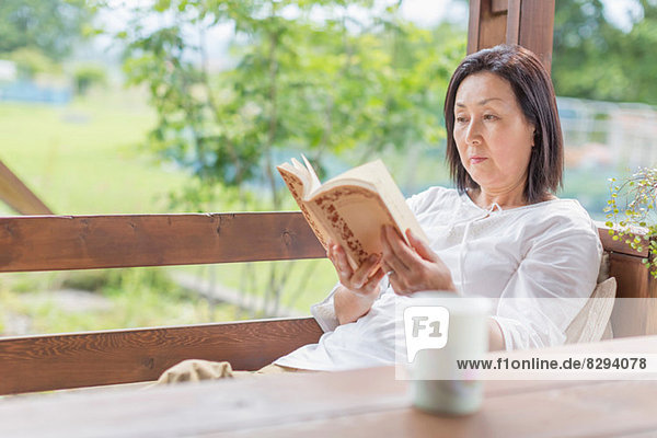 Frau liest Buch auf der Terrasse