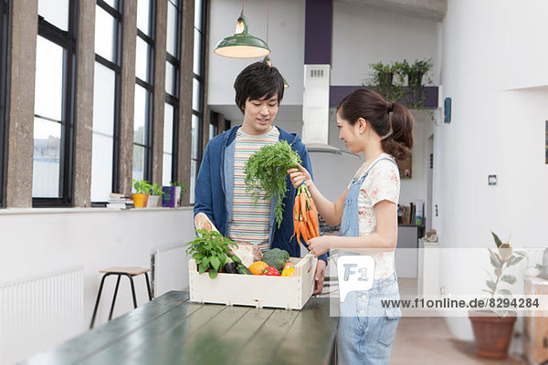 Junges Paar in der Küche mit Gemüsekiste mit Karotten