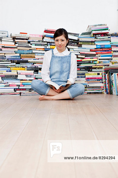 Junge Frau mit gekreuzten Beinen auf dem Boden vor dem Bücherstapel