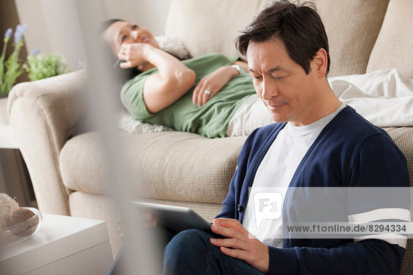 Mature man using digital tablet  woman lying on sofa