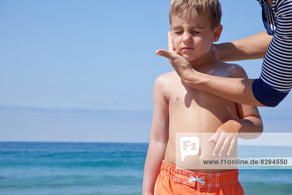 Mutter trägt Sonnencreme auf das Gesicht der Söhne am Strand auf.