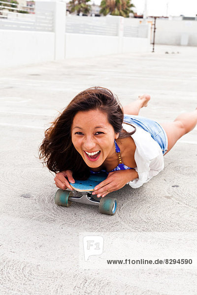 Woman in parking lot lying on skateboard