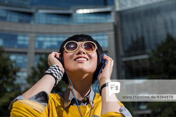 Young woman wearing sunglasses and headphones looking up