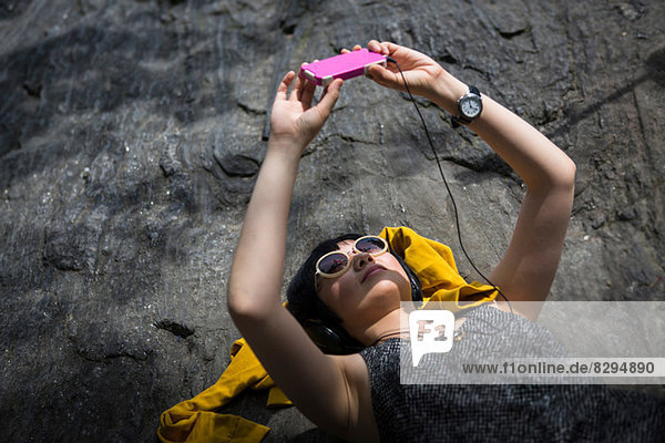 Young woman lying on rocks listening to mp3 player