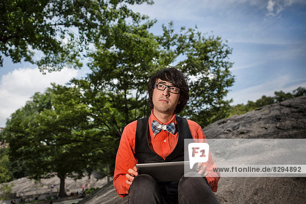 Junger Mann auf Steinen sitzend mit Tablette