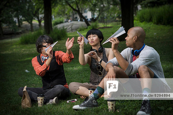Three friends holding paper planes in park